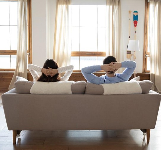 GHS AQT View from Behind of a Woman and a Man Sitting on a Couch Looking at a Window with Their Hands Crossed Behind Their Heads