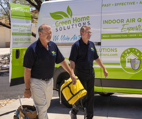 two men in Green Home Solutions uniform walk in front of their van while carrying equipment