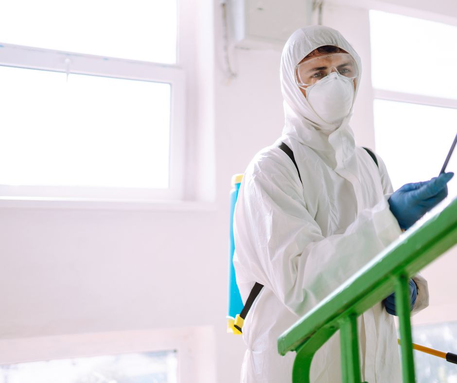 Green Home Solutions of West Virginia Disinfection Service man in white hazmat suit spraying a disinfection solution with a wand