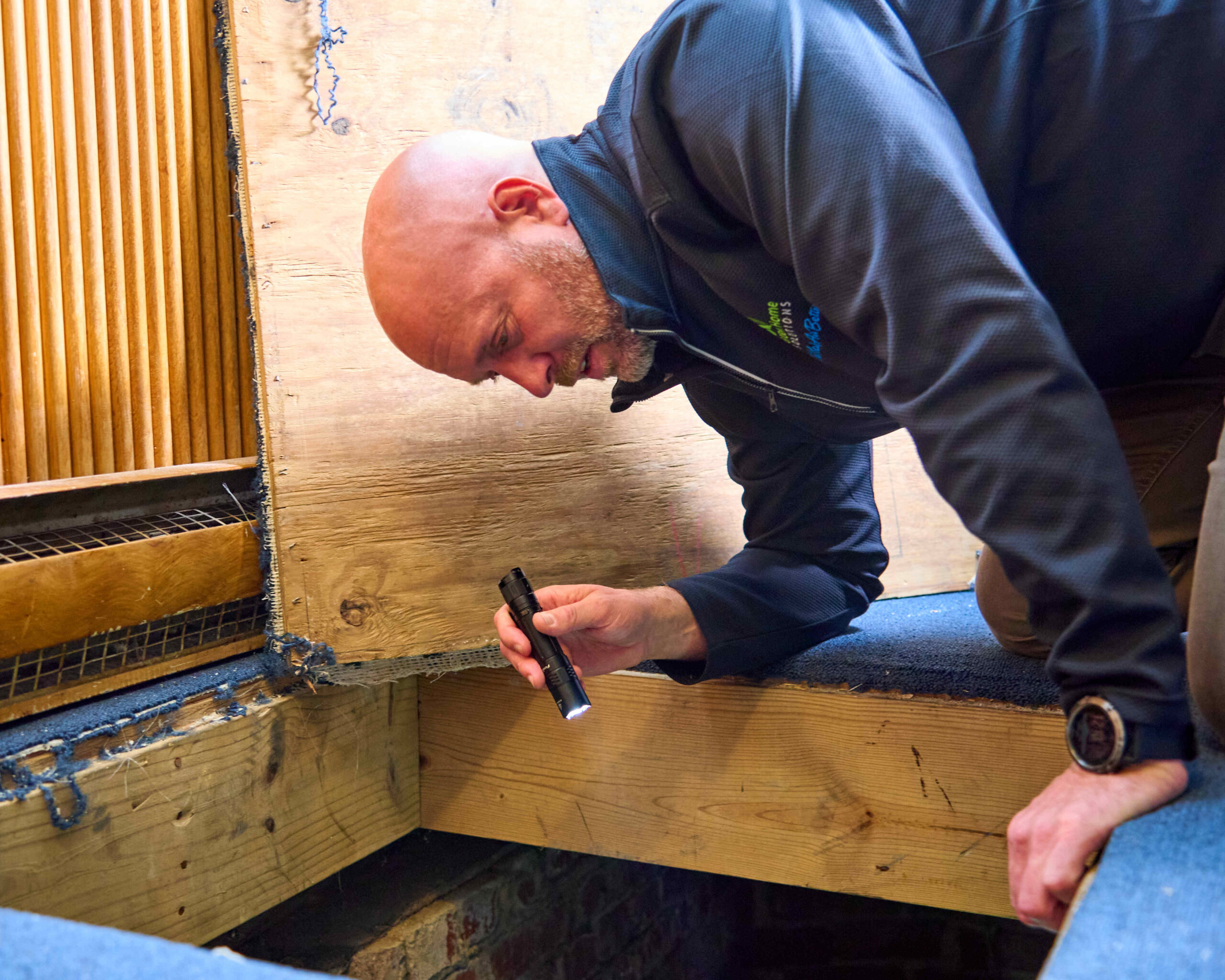 inspector looking at a crawlspace in the floor with a flashlight checking for mold or other dangers