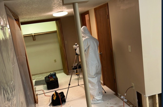 A man in a white suit and coveralls stands in a hallway, ready for mold remediation work