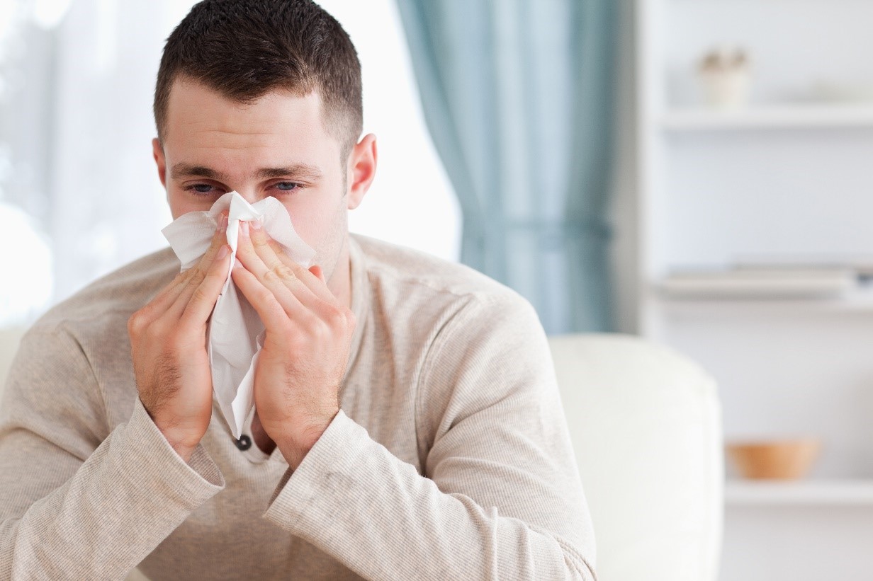 A Man in a Beige Long-Sleeve Shirt Blowing His Nose into a Tissue