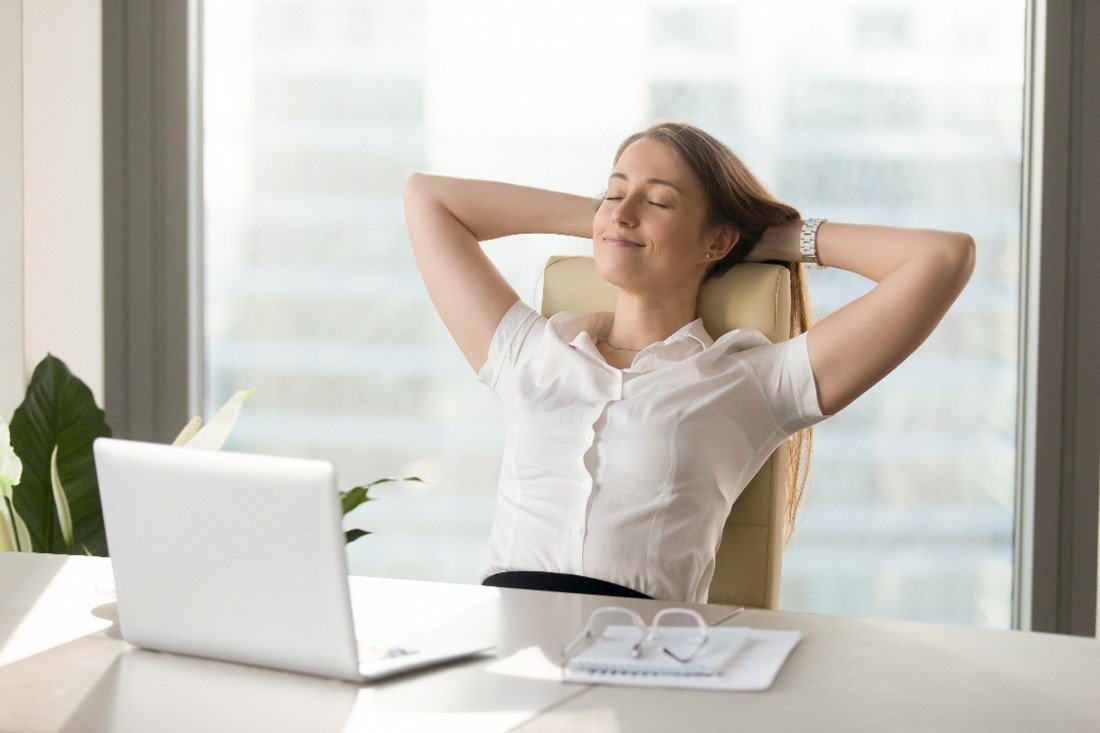 service8 A woman who is lightly smiling leans back in a chair at a desk with her eyes closed and her hands clasped behind her head.