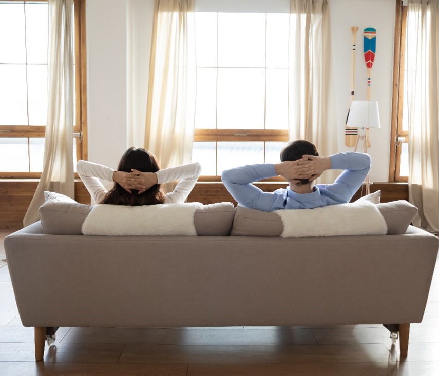 View from Behind of a Woman and a Man Sitting on a Couch Looking at a Window with Their Hands