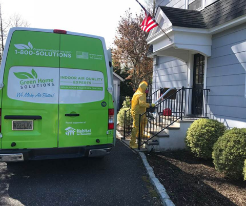 Rear Doors of a Green Home Solutions Van Parked A Woman Sits at a Desk with an Open Laptop and Leans Back with Her Eyes Closed and Arms Behind Her Head Taking a Deep Breath