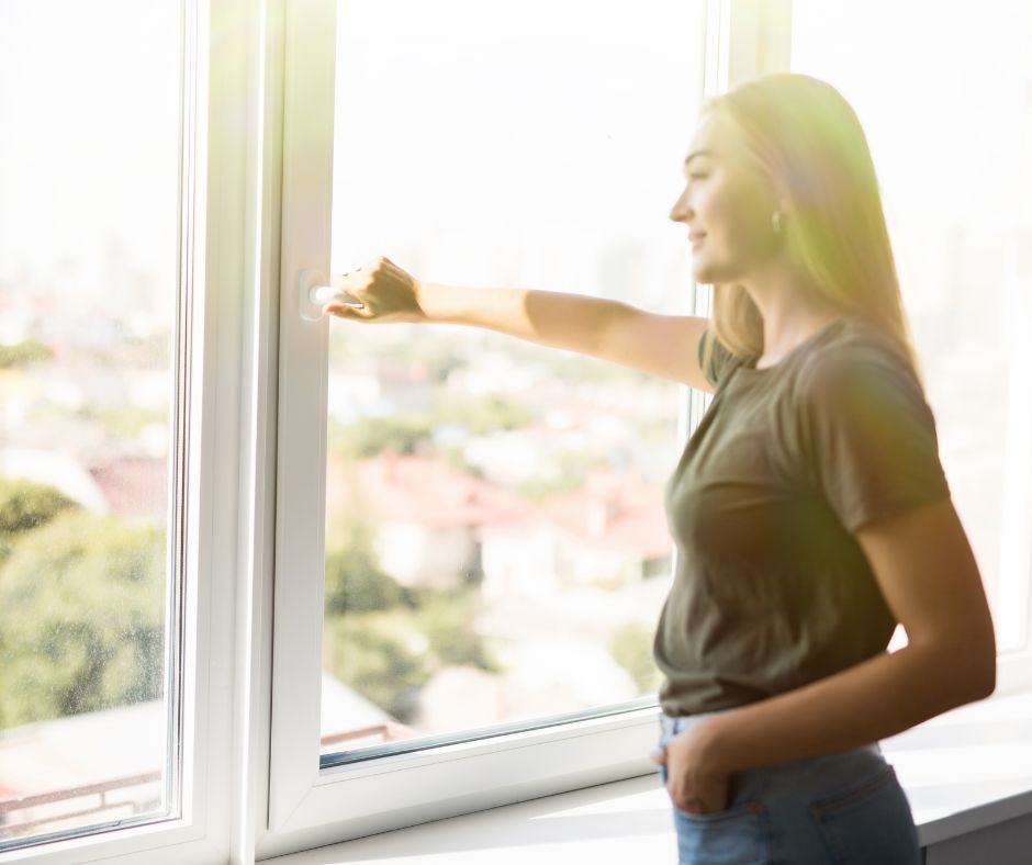 Green Home Solutions Indoor Air Quality A woman wearing a denim jacket, holding her nose while spraying an air freshener in front of a yellow background.