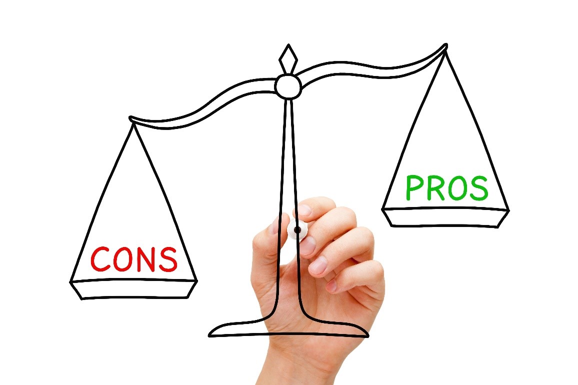 A hand drawing a scale with one side labelled PROS outweighing the other side labelled CONS. 