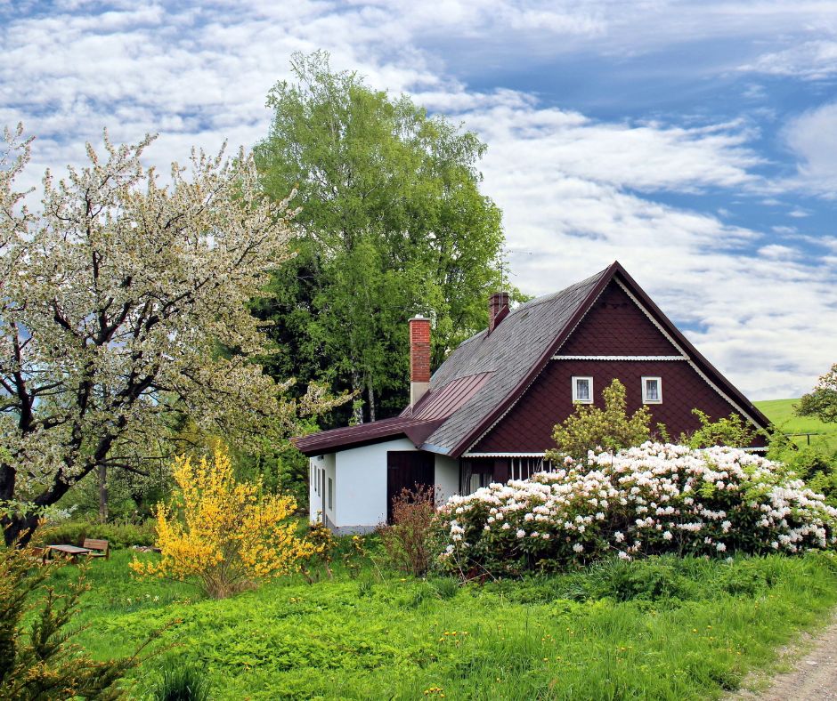 a small brown house surrounded by spring flowers and green grass