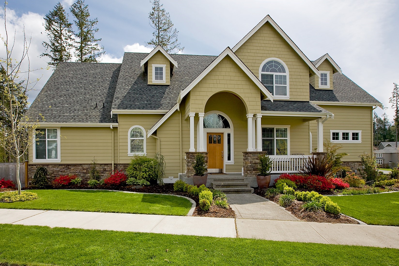 A picture-perfect ochre colored home with a pointed roof surrounded by a green, neat lawn.