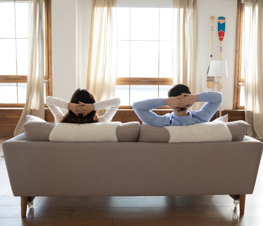 View from Behind of a Woman and a Man Sitting on a Couch Looking at a Window with Their Hands Crossed Behind Their Heads